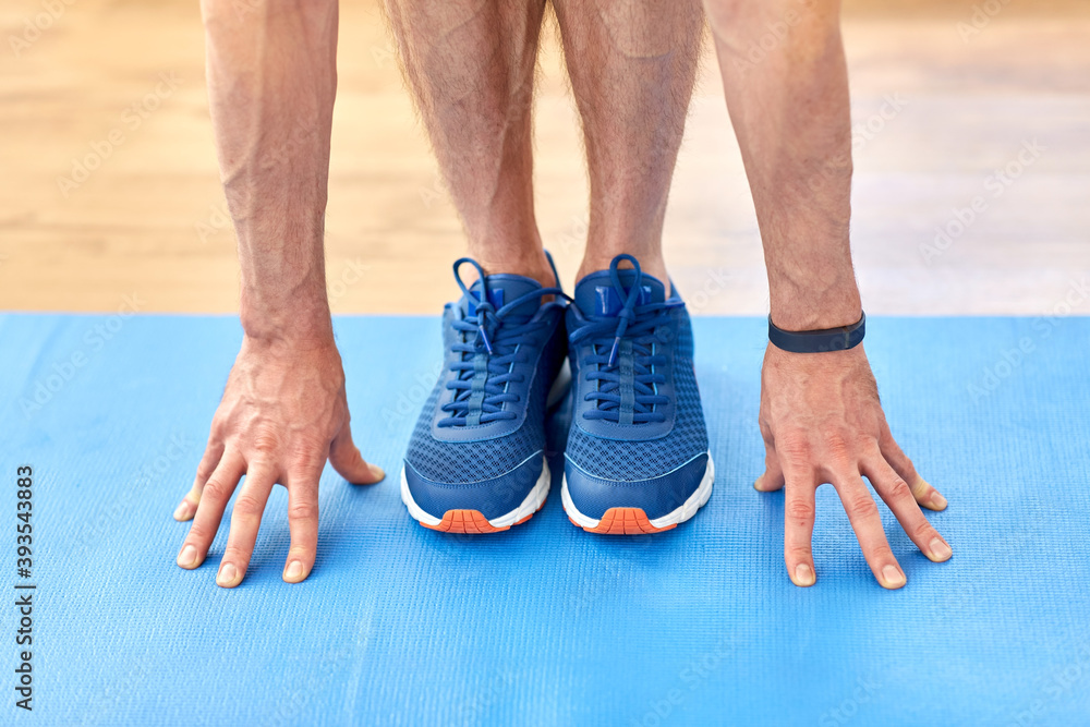 fitness, sport and footwear concept - close up of male hands and feet in blue sneakers on exercise mat fitness, sport and footwear concept - close up of male hands and feet in blue sneakers on exercise mat