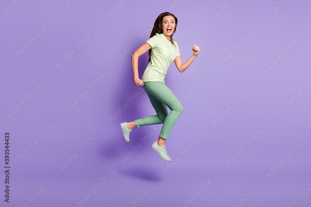 Full body profile photo of impressed ecstatic person open mouth shout run jump wear green isolated on violet color background