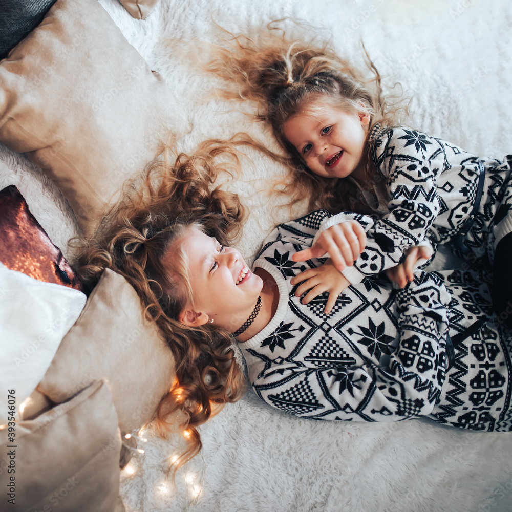 Children playing on a large bed. Friendly family concept. In the background there are lights from a garland Children playing on a large bed. Friendly family concept. In the background there are lights from a garland