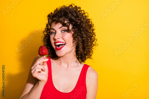 Photo of charming pretty lovely tempted curly red lipstick lady eat enjoy summer season fruits hold hand berry open mouth wear red tank top isolated yellow color background