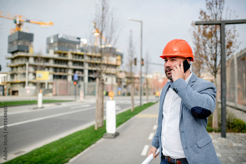 Young architect holding mobile phone and blueprint while looking away. Young architect holding mobile phone and blueprint while looking away.