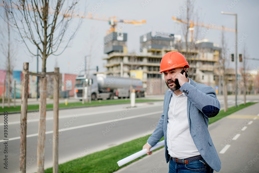 Young architect holding mobile phone and blueprint while looking away. Young architect holding mobile phone and blueprint while looking away.