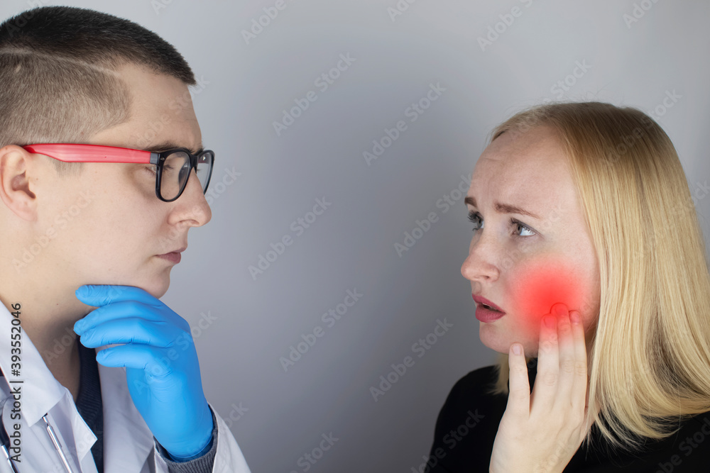 A woman clings to his cheek and winces in pain in his tooth. The concept of dental problems, caries, tooth decay, flux. White background and place for text. On examination by a doctor. A woman clings to his cheek and winces in pain in his tooth. The concept of dental problems, caries, tooth decay, flux. White background and place for text. On examination by a doctor.
