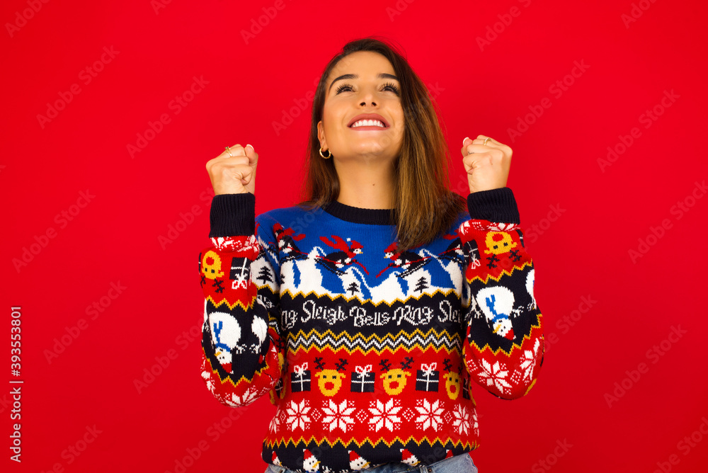 Young Young beautiful Caucasian woman wearing Christmas sweater against red wall, having success being glad to achieve his goals. Victory and triumph concept. Young Young beautiful Caucasian woman wearing Christmas sweater against red wall, having success being glad to achieve his goals. Victory and triumph concept.