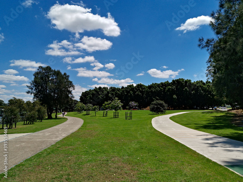 Beautiful view of a park with with twin paved trail for walking and cycling, green grass, tall trees and blue sky, Reid Park, Parramatta Cycleway, Rydalmere, Sydney, New South Wales, Australia
