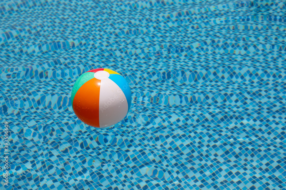 Beach ball in pool. Colorful inflatable ball floating in swimming pool, summer vacation concept.