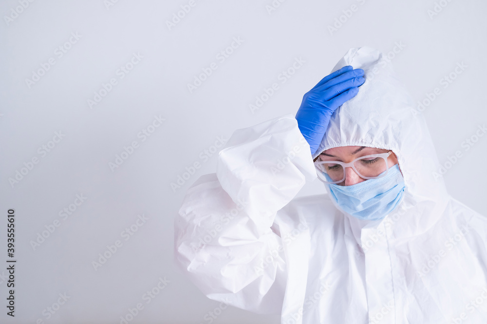 A woman in a protective suit and a medical mask is holding her head. Doctor virologist with problems at work A woman in a protective suit and a medical mask is holding her head. Doctor virologist with problems at work