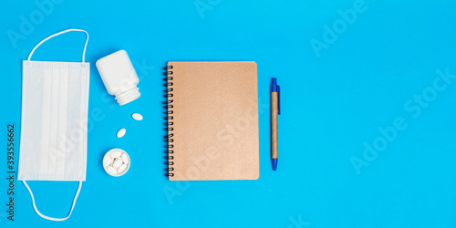 White medical mask, bottle with pills and notepad on blue background. Concepts of protection, prevention and treatment coronavirus, covid 19, flu. top view