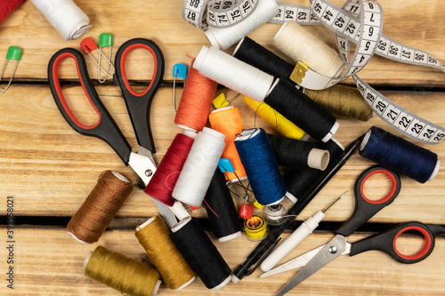 Sewing tools and accessories for sewing - colored threads, spools, scissors, pin and tailor meter on a wooden background