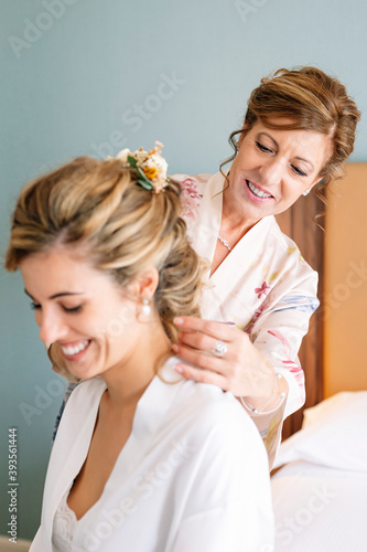 Beautiful blonde haired woman dressed in white on her wedding day before getting married  her mother helps her get dressed.