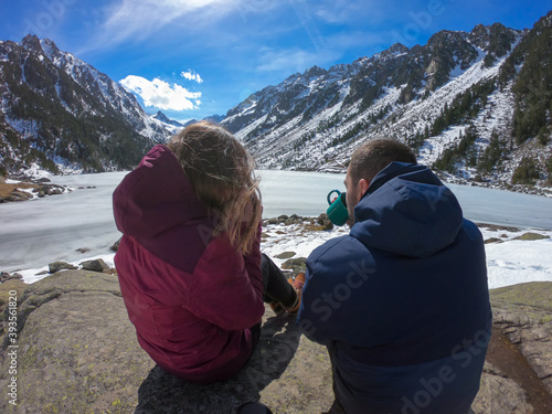 Couple drinking hot coffee or tea and sitting next to stunning winter landscape. Concept of travel and adventure at the frozen Gaube Lake (Lac de Gaube) in the French Pyrenees, France.