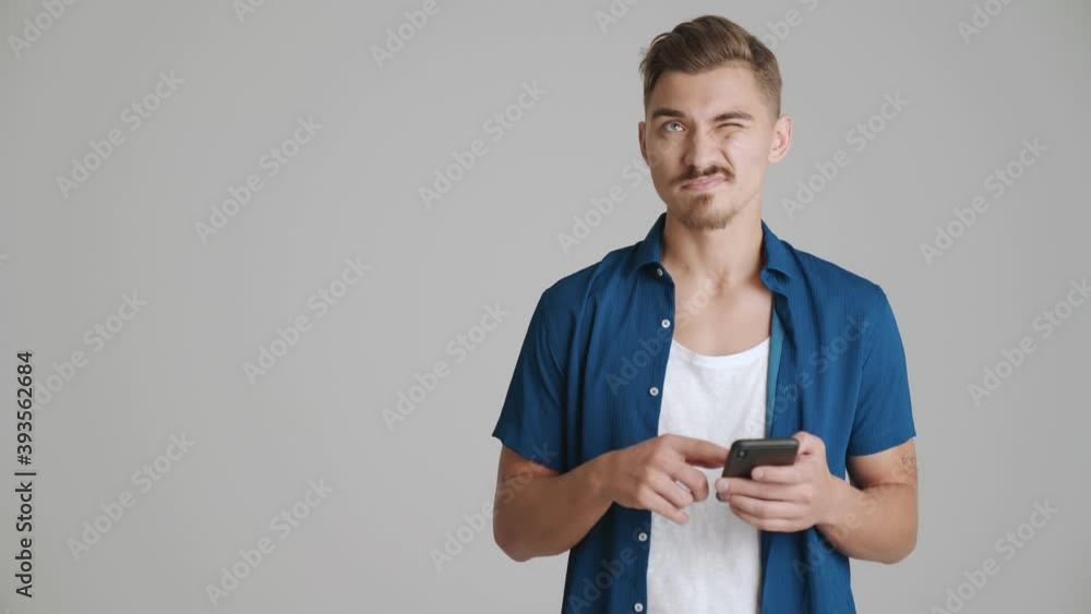 A serious man is using his smartphone standing isolated over gray background in studio A serious man is using his smartphone standing isolated over gray background in studio
