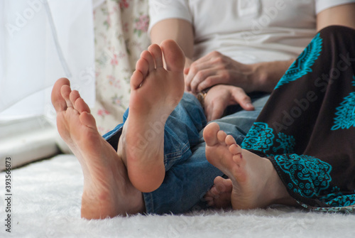 young couple in casual clothes is sitting at home on the floor before the windows. Bare feet in focus. View of a couple's feet