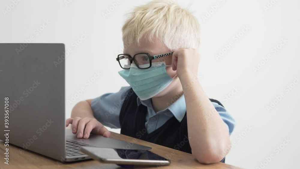 A boy schoolboy with glasses and a medical mask on his face is engaged in school on a computer. A boy schoolboy with glasses and a medical mask on his face is engaged in school on a computer.