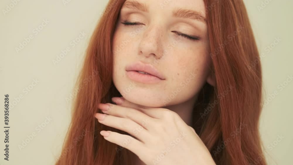 A nice woman is posing to the camera while touching her face standing isolated over beige background in studio A nice woman is posing to the camera while touching her face standing isolated over beige background in studio
