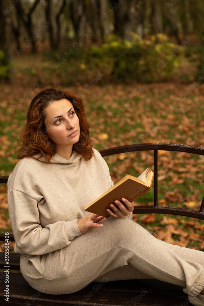 Obraz premium a young beautiful girl is sitting on a bench in an autumn Park, reading a book 