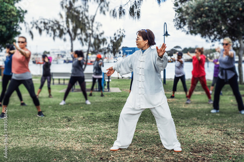 Mature chinese woman do tai chi with blirred group of people outdoor in the park photo