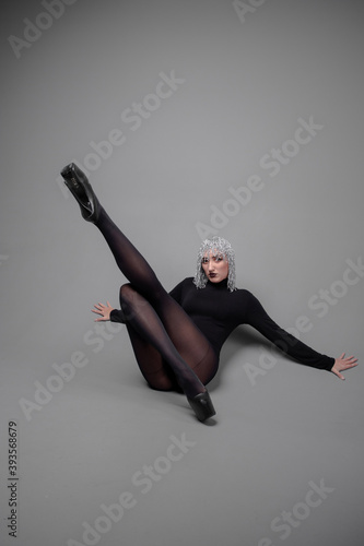 a long-legged girl in a silver wig in a black bodysuit and stockings in a photo studio in unusual poses on a gray background