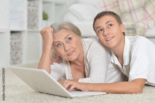 Grandmother with her grandson using laptop on carpet at home
