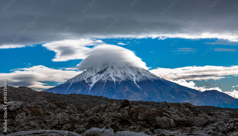 View of the top of the volcano, covered with a cloud cap. Lava field in the foreground