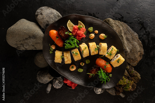 A set of sushi on a beautiful black plate. Japanese dish. Sushi rolls with Japanese tamago amlet and salmon sashimi with rice, gunkans with red caviar, ginger, wasabi, chuka salad and peanut sauce. photo