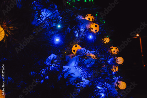 Christmas lights in the form of soccer balls shine at night in the yard. Christmas tree decorated with yellow and blue lights, closeup.