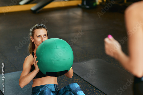 Young sportive woman in sportswear doing abs exercises exercising with fitness ball at gym with assistance of personal trainer © Friends Stock