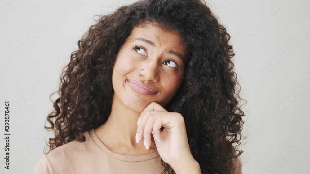 A close-up view of an attractive african american woman is thinking about something standing isolated over beige background A close-up view of an attractive african american woman is thinking about something standing isolated over beige background
