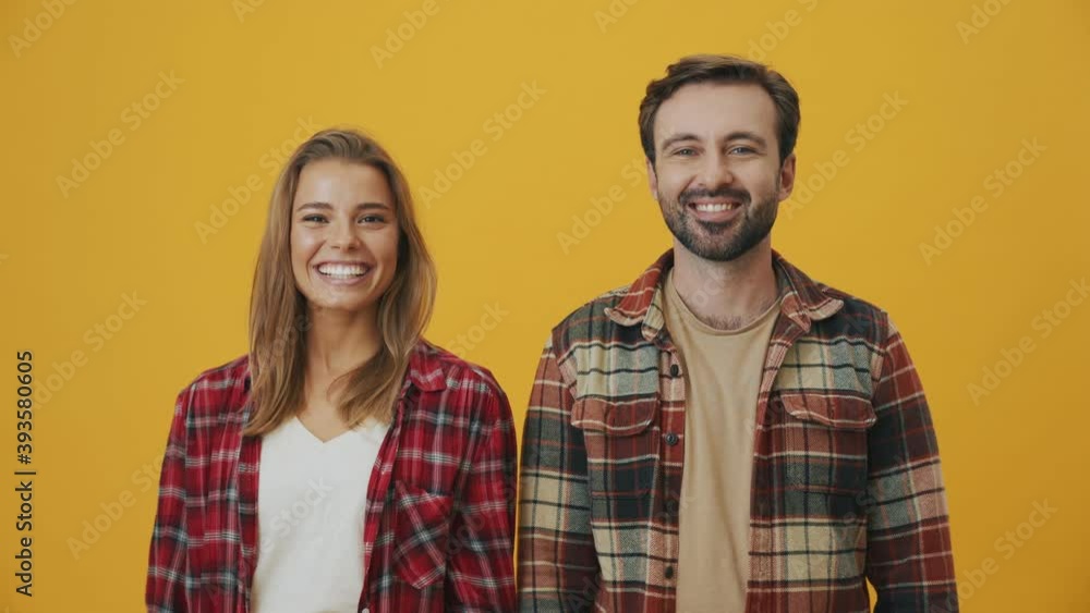 A happy couple man and woman are smiling to the camera standing isolated over yellow background A happy couple man and woman are smiling to the camera standing isolated over yellow background
