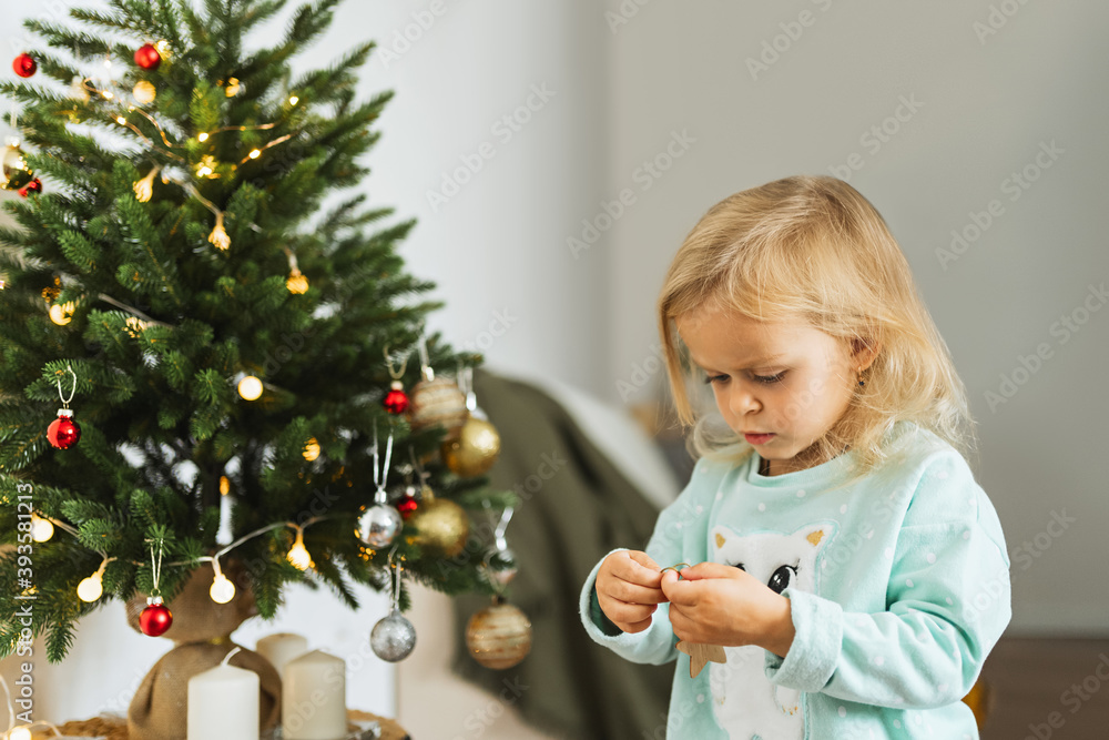 .A cute little girl in pajamas decorates a Christmas tree with balls in the room. Merry christmas and happy new year concept. Space for text. Family cozy moments. .A cute little girl in pajamas decorates a Christmas tree with balls in the room. Merry christmas and happy new year concept. Space for text. Family cozy moments.