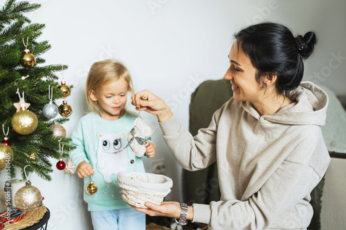 Mom and daughter decorate the Christmas tree in room.  Merry christmas and happy new year concept. Space for text. Family cozy moments. photo