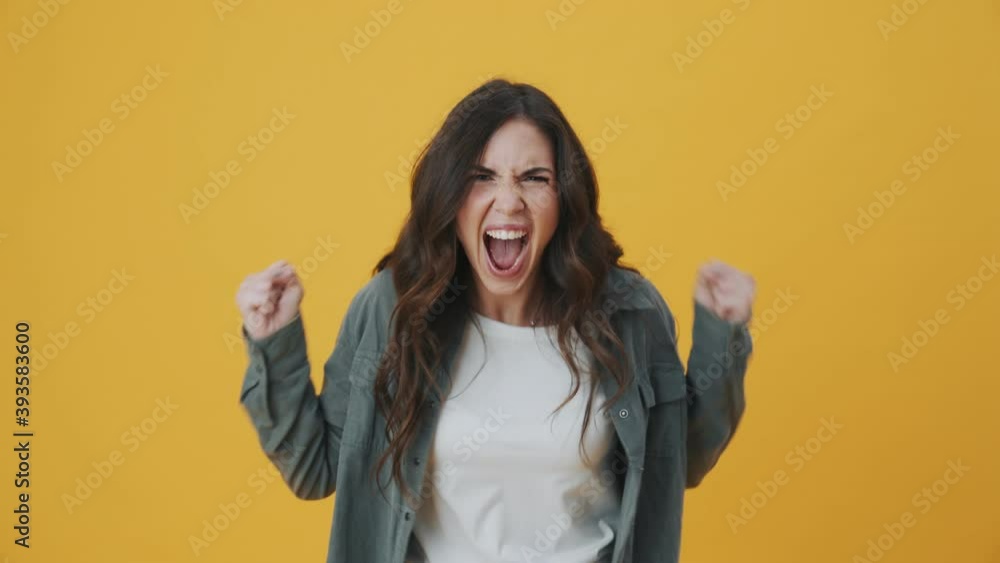 An angry woman is screaming while standing isolated over yellow background An angry woman is screaming while standing isolated over yellow background
