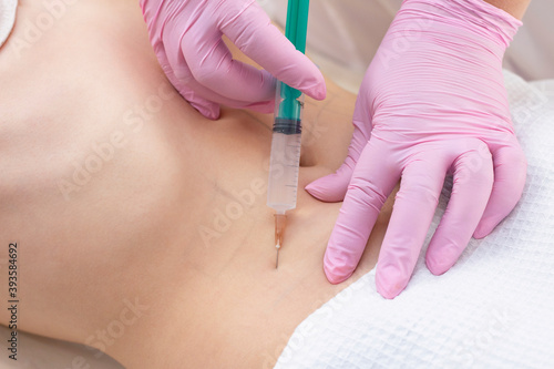 lipolytic injections are placed in the stomach. female hands in pink gloves inject a young woman into the stomach.