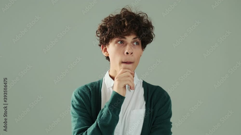 An attractive young man is thinking about something and raising his finger standing isolated over a grey wall in studio An attractive young man is thinking about something and raising his finger standing isolated over a grey wall in studio