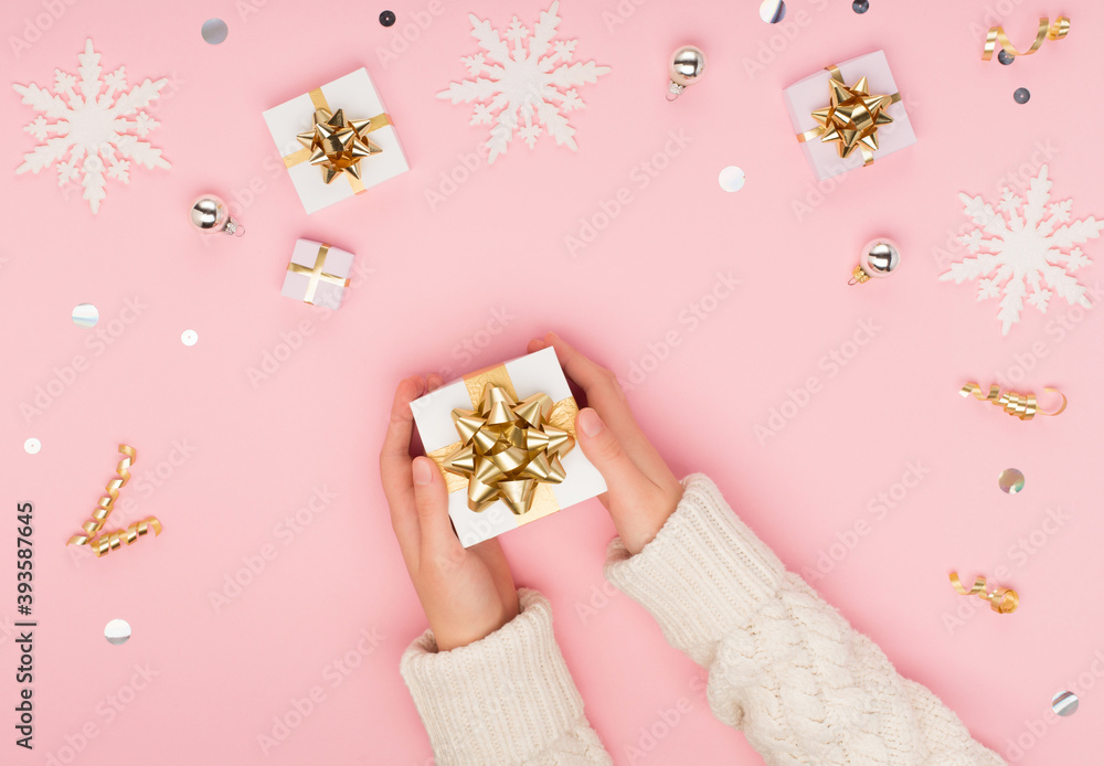 Top view on female hands holding white gift box wrapped with gold bow on Christmas pink background. Top view on female hands holding white gift box wrapped with gold bow on Christmas pink background.