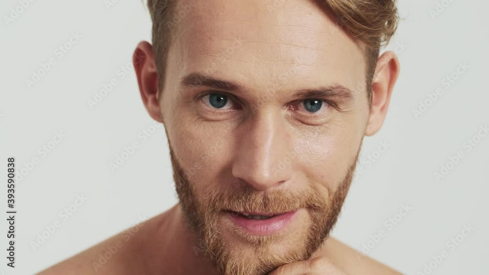 A close-up view of an attractive blonde man is smiling to the camera standing isolated over a grey background in the studio A close-up view of an attractive blonde man is smiling to the camera standing isolated over a grey background in the studio