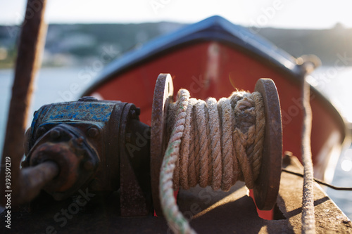 Canvas Print Rusty winch with rope on fishing boat deck, red boathouse in background
