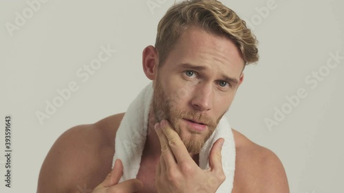 A good-looking half-naked blonde man is looking to the camera like to the mirror standing isolated over a grey background in the studio photo