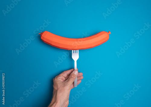 Hand holding sausage made of paper with a spoon (ID: 393591872)
