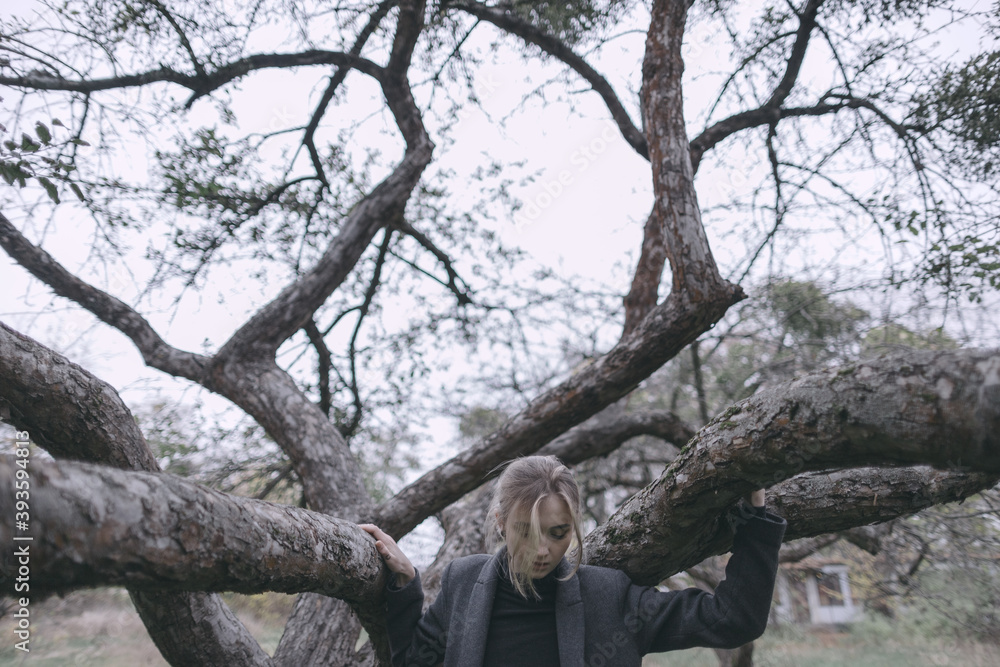 Scandinavian girl in gray casual modern clothes dancing a ritual dance by a tree in Uppsala pulling her hands up on her face blonde curls falling