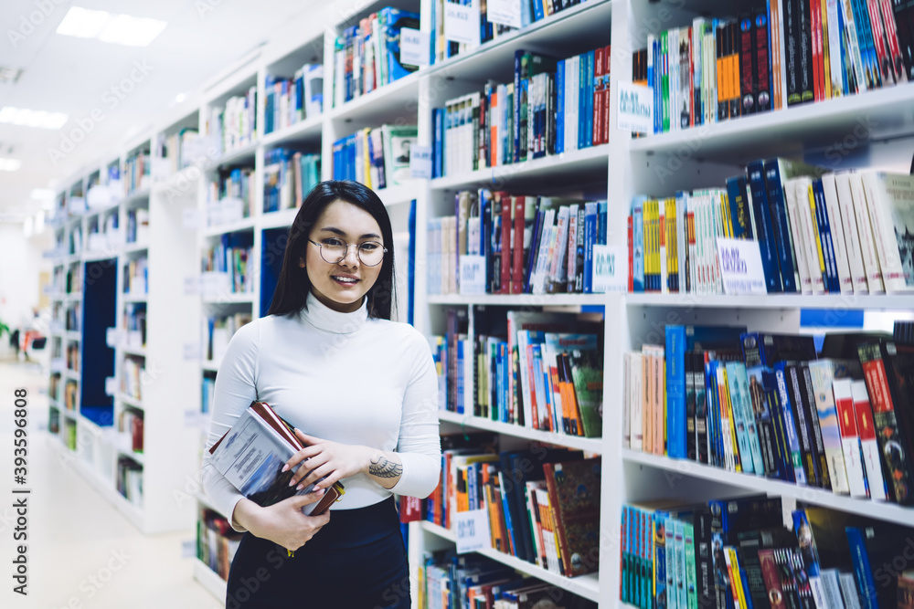 Asian female student with books walking in library Asian female student with books walking in library