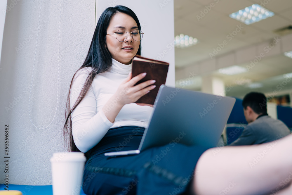 Young Asian woman sitting with laptop and holding notebook Young Asian woman sitting with laptop and holding notebook