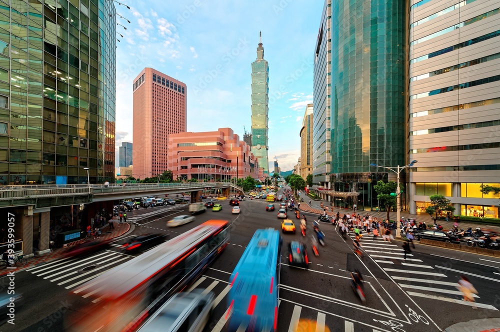 Obraz premium View of a busy street corner in Downtown Taipei City at rush hour with cars & buses dashing by, Taipei 101 Tower & World Trade Center Building in Xinyi Financial District & people passing on crosswalk