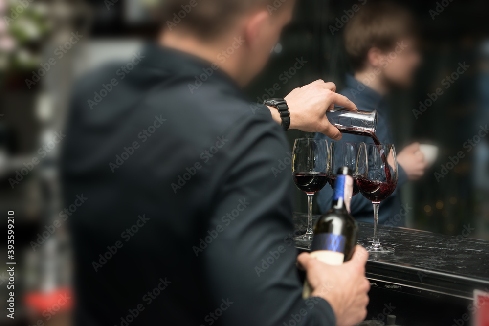 Barman pouring red wine into glasses in detail