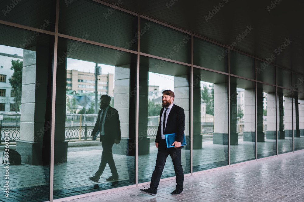 Fototapeta premium Positive businessman walking along glass wall