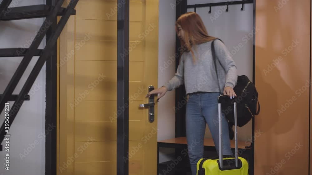Confident charming teenage girl entering hotel room with backpack and yellow travel bag. Portrait of happy Caucasian beautiful teenager travelling or studying abroad. Tourism and lifestyle. Confident charming teenage girl entering hotel room with backpack and yellow travel bag. Portrait of happy Caucasian beautiful teenager travelling or studying abroad. Tourism and lifestyle.