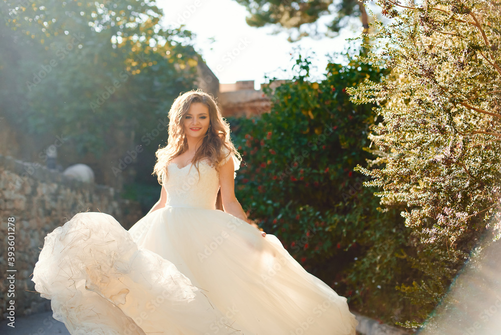 Beautiful stylish bride in a white dress. Posing against the backdrop of green bushes. Beautiful backlight