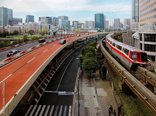 Scenery of a train traveling on the elevated Monorail near Tennozu Isle Station in Tokyo, Japan and cars driving on an expressway curve with Tokyo Tower standing amid high rise buildings in background photo