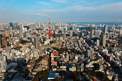 An aerial panorama from Roppongi over Downtown Tokyo, with landmark Tokyo Tower among crowded buildings, city streets crisscrossing the district & Tokyo Bay on distant horizon on a beautiful sunny day