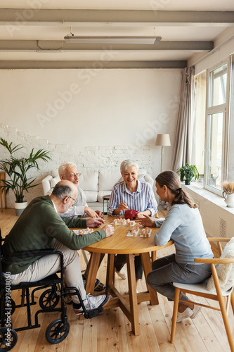 Group of four friendly senior people, two men and two women, sitting at table and enjoying playing bingo game in nursing home